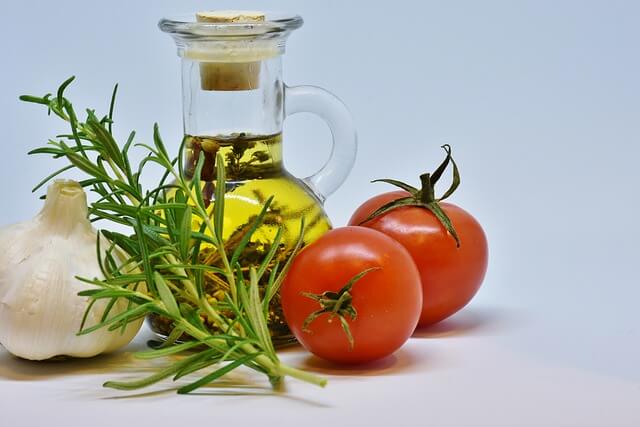 Une fiole remplie d'huile, des tomates, de l'aïl et du romarin